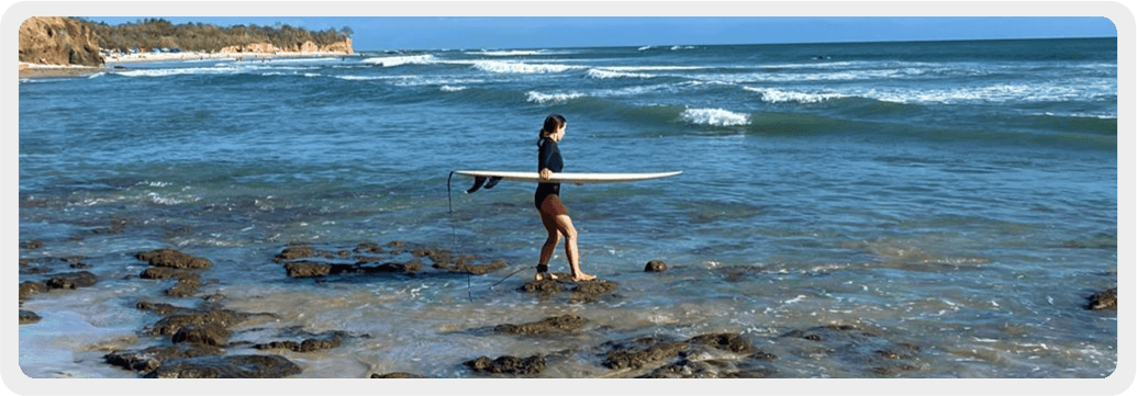 Nikki Costello carrying a surfboard into the ocean